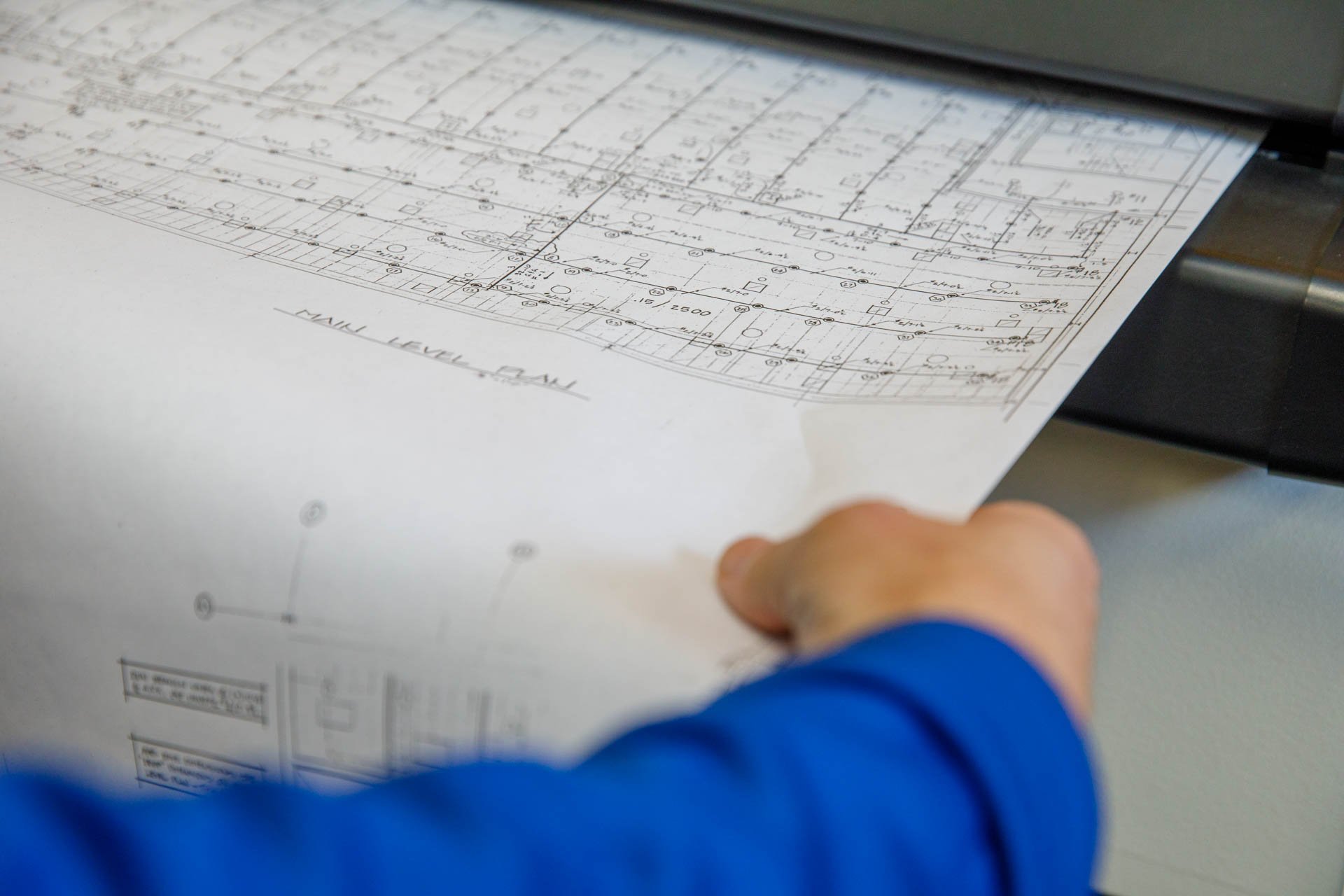 an image of an original government building blueprint being fed into a large format scanner in eo johnson's scanning office
