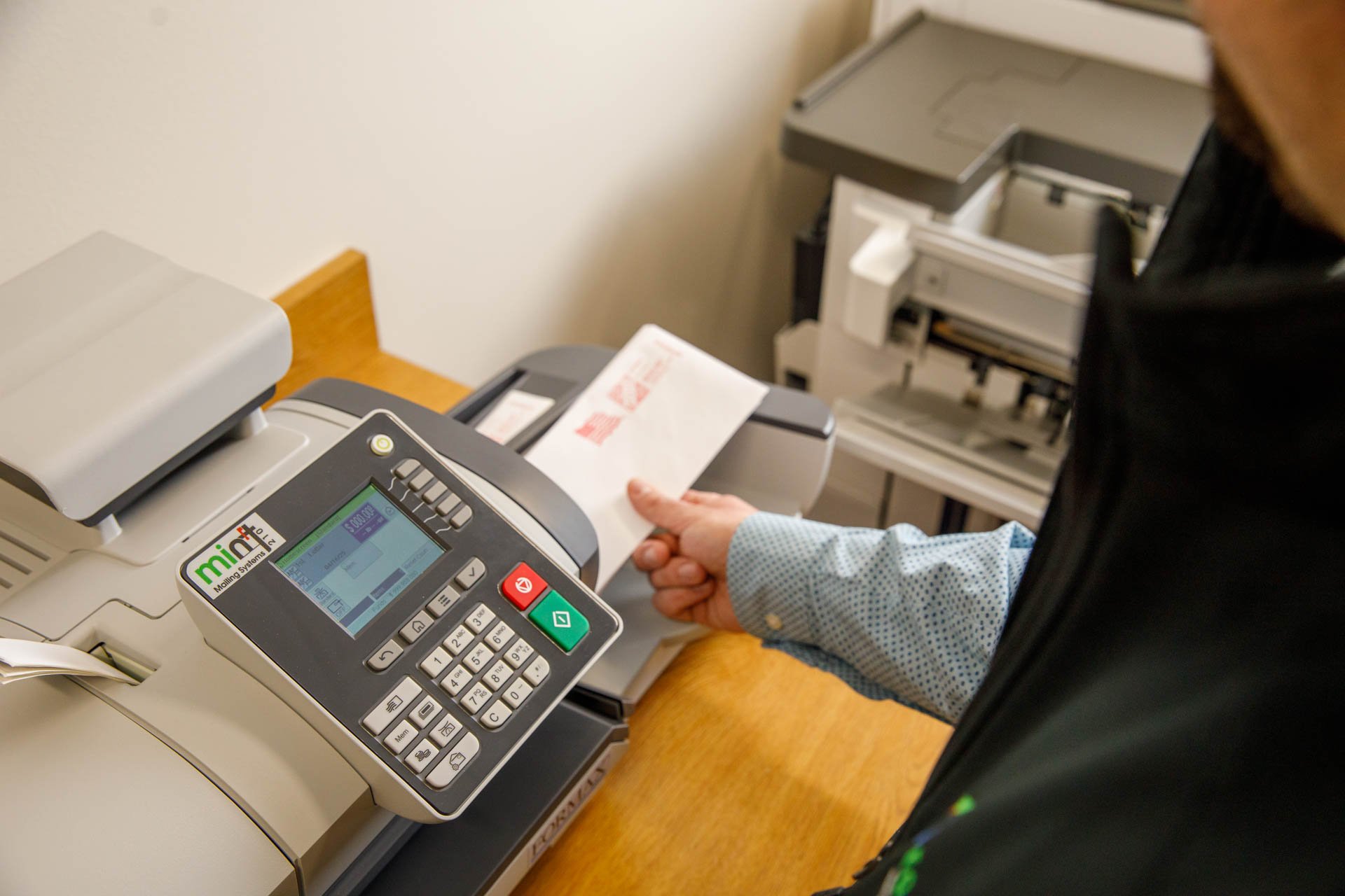 an image of a professional grabbing an envelope out of a mint 210 mailing system with postage on it