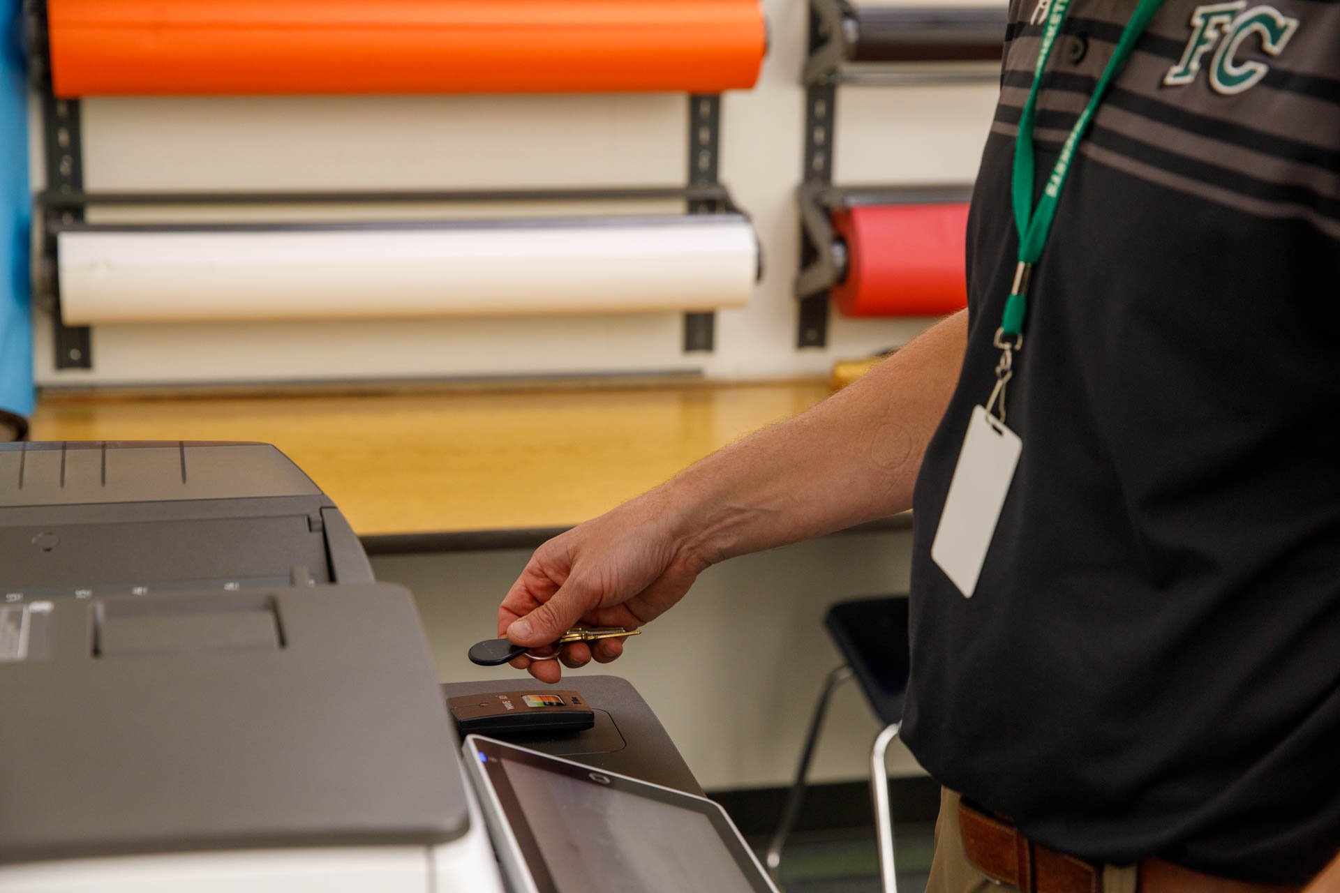 An image of a teacher using his fob to gain access to a print job on a printer in a school copy room