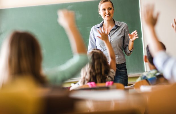 an image of a teacher looking for a student to call on as they all raise their hands.
