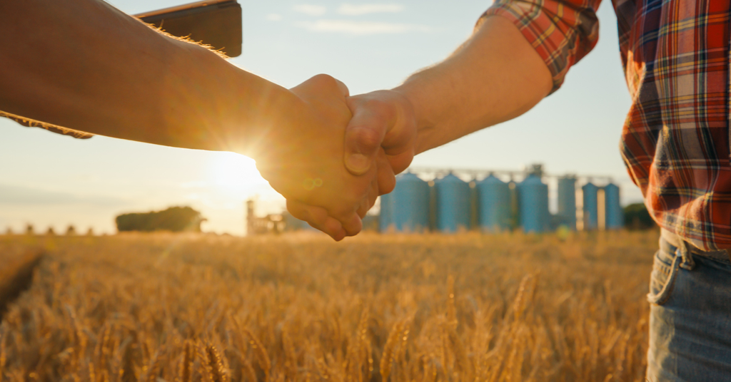 an image of a farmer shaking hands with a cell phone in the other showing file accessibility even in the middle of a wheat field.