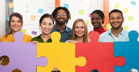 an image of a group of employees smiling at the camera while holding interconnecting puzzle pieces together